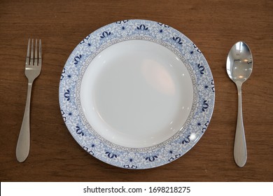 White round with blue rim Plate between spoon and fork on Wooden top table - Shutterstock ID 1698218275