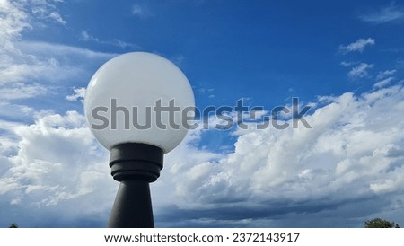 White round lantern with black base pole on a beautiful sky background filled with clean white clouds. 