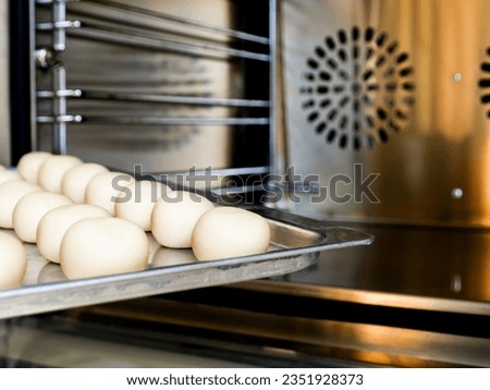 white round pastry dough arranged in a row in a stainless steel tray Putting into a large baking oven, the baking concept