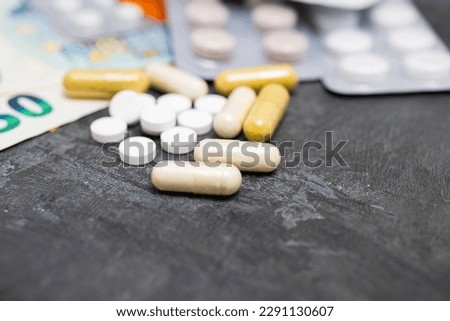 White round pills, capsules, blister packs with tablets, antibiotic, painkiller or drugs and money, Euro currency banknotes, expensive medicine and healthcare concept, close-up view.
