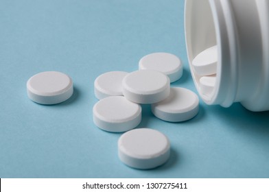 White Round Pills Spilling Out Of The Medicine Bottle On Blue Background; Safe Drug Use And Healthcare Business Concept. Closed Up And Selective Focus