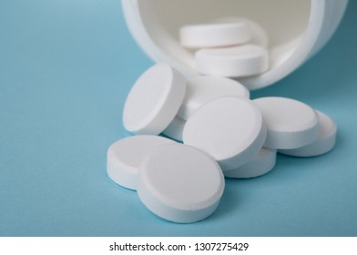 White Round Pills Spilling Out Of The Medicine Bottle On Blue Background; Safe Drug Use And Healthcare Concept. Closed Up And Selective Focus