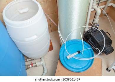 White Round Plastic Water Tank For Osmosis Water Purification System. Nearby Lies A Blue Lid And A Black Pump

