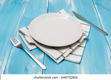 White Round Plate With Utensils And Dish Towel On Ocean Blue Wooden Table Background With Perspective