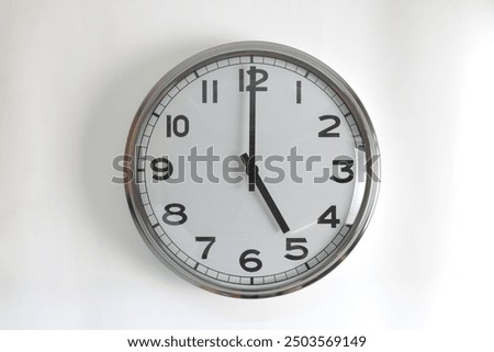 A white round shape wall clock with black hands showing the time of 5 o'clock cutout from background. Short hand at 5 o'clock and long hand at number 12.