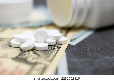 White round therapeutic pills for treatment, painkiller or drugs with money, US dollar banknotes, expensive medicine and healthcare concept, close-up view. - Powered by Shutterstock