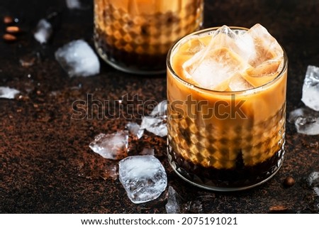 White russian cocktail, trendy alcoholic drink with vodka, coffee liqueur, cream and ice, dark background, bar tools