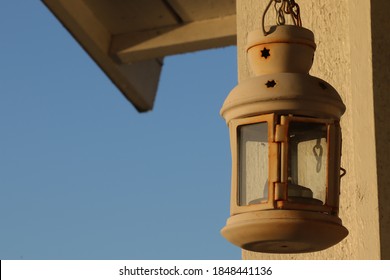 A white rusty rustic candle lantern hanging from a chain lit by sunrise