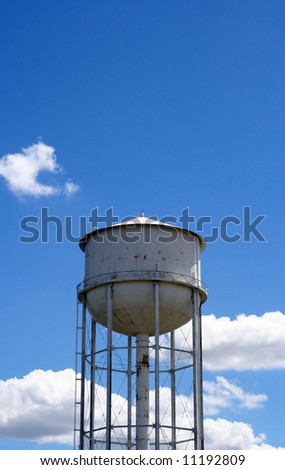 A white rusty watertower against a blue cloudy sky.