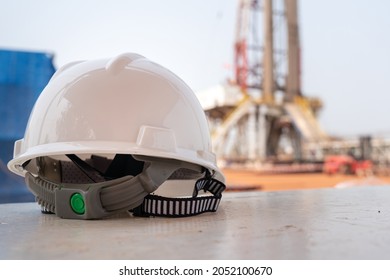 A White Safety Hardhat With Blurred Background Of Drilling Rig Derrick Structure. Heavy Industrial, Ready For Working In Challenge Concept Photo. Close-up And The Object. 