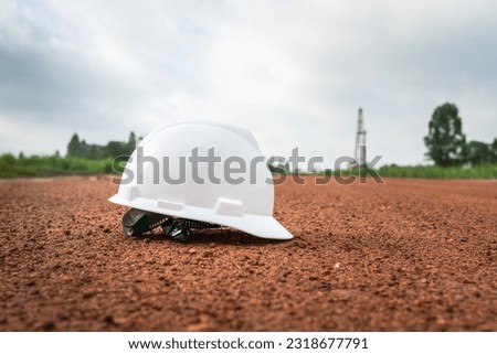 A white safety helmet or hardhat of construction worker is placed on terrain ground with background of the onshore drilling rig as far away. Industrial safety PPE object.
