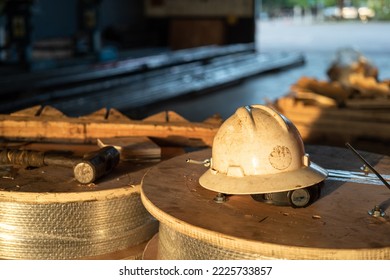 A White Safety Working Hardhat Or Helmet In Orange Sun Lighting Which Is Placed On The Material Wooden Reel Ac The Factory. Industrial Safety Equipment Object. Close-up And Selective Focus.