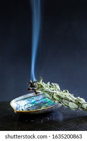 White sage smudge stick on dark background. Burning / smudging sage on abalone shell. Native American tradition for cleansing negative energy.