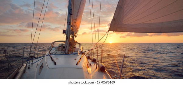 White sailboat in an open sea at sunset. Single handed sailing a 34 ft yacht. Close-up view of the deck, mast and sails. England, UK. Colorful dramatic cloudscape. Sport, racing, recreation - Powered by Shutterstock