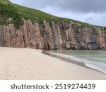 White sand beach meets rock cliff face on a cloudy day