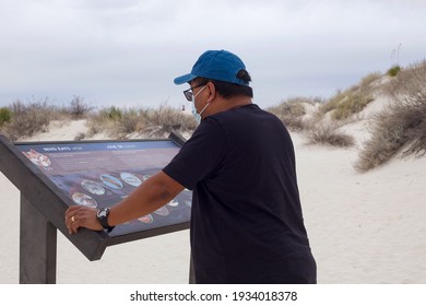 White Sands, New Mexico - USA - March 9, 2021: An Asian Man Wearing A Mask During The Covid-19 Pandemic Is Reading A Sign On The Dune Life Nature Trail In White Sands National Park.