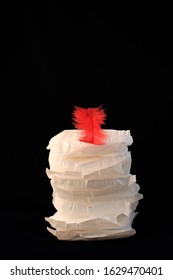 White Sanitary Individually Wrapped Napkin Pads In Stack With Red Feather On Top, Black Background. Menorrhagia, Heavy Menstruation. Menstrual Critical Days Hygiene. Irregular Period Creative Concept.