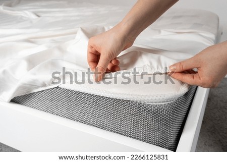 A white satin sheet with an elastic band is put on the mattress of the bed, a close-up of the hands. Bedclothes.
