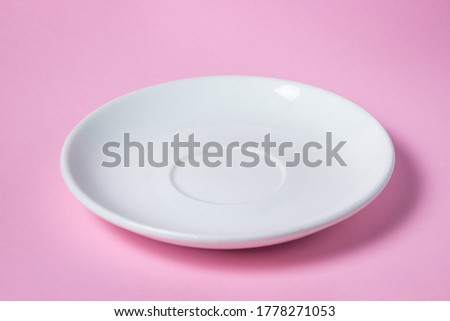 White saucer on a pink background. Empty white porcelain saucer stands on a pink surface