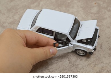 White scale model with open hood, door, and trunk revealing detailed engine bay. A hand adjusts the interior with small tools. Perfect for diecast hobbyists, automotive collectibles, and vintage car photography.