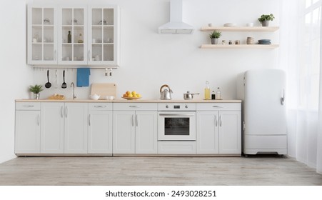 White scandinavian kitchen interior with dining room and wooden floor. Simply furniture with utensils, shelves with crockery and plants in pot, refrigerator in modern minimal design, empty space