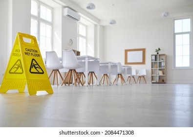 White School, College Or University Classroom With Row Of Desks And Chairs Where Janitorial Or Cleaning Service Worker Placed Plastic Sign With Figure That Slips And Falls And Words Caution Wet Floor