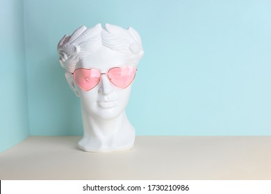 White sculpture of an antique head in pink glasses with hearts. On a geometric background of two colors