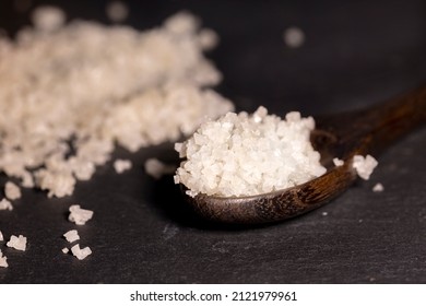 White sea salt crystals and wooden spoon on a black slate background