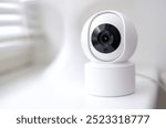 A white security camera with a black lens is mounted on a white surface. The camera is designed to capture images and record video footage