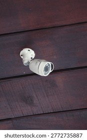 A white security camera mounted on a dark wooden wall for surveillance and safety
