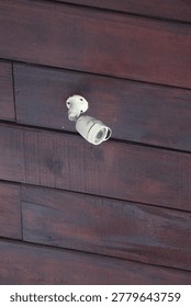 A white security camera mounted on a dark wooden wall for surveillance and safety
