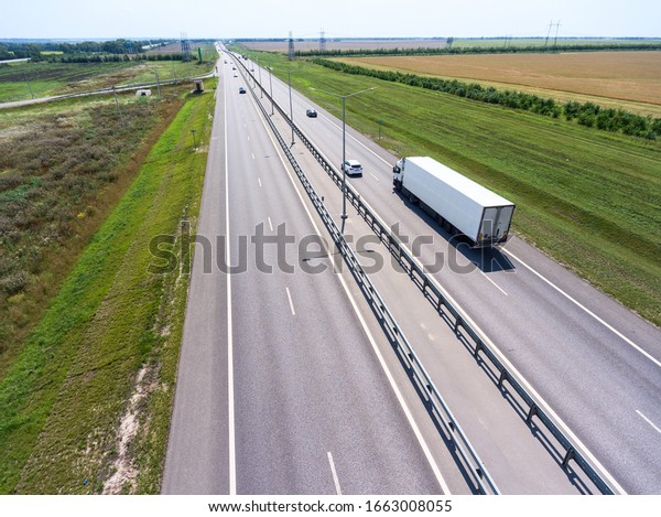 White\
semi trailer truck driving on wide straight highway in agricultural\
fields. View from above. The Don M4 route in\
Russia