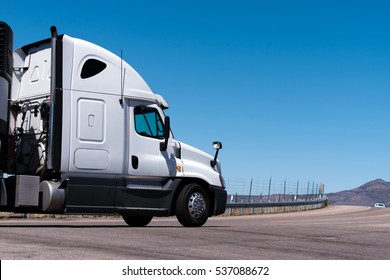 White Semi Truck Going On The Road With Road Fence, Mountain And Blue Sky