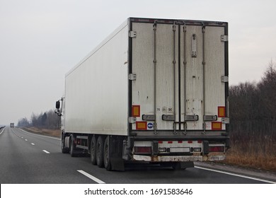 White semi truck van move on suburban asphalted highway road at spring day, rear-side view close up – international logistics, cargo transportation, trucking industry