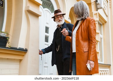 White Senior Couple Holding Hands And Smiling While Standing By Door Outdoors