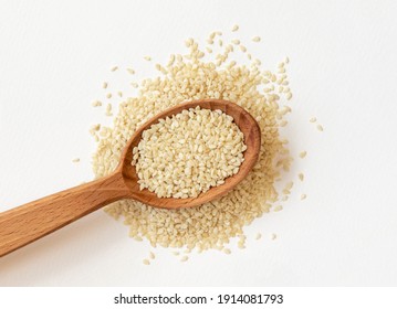 White sesame seeds in wooden spoon on pile of white sesame seeds, top view.