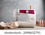 White sewing machine with beige fabric and craft accessories on wooden table near gray wall