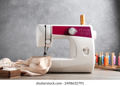 White sewing machine with beige fabric and craft accessories on wooden table near gray wall