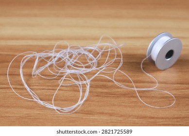 White Sewing Thread Spool with Tangled Thread on Wooden Table Close Up Craft and Tailoring Concept