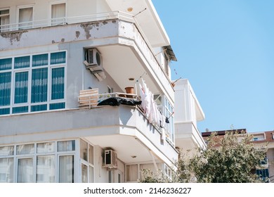 White shabby rundown residential building with drying clothes on the balcony. Simple people living. Scuffed worn-out residential block with old air conditioning system.