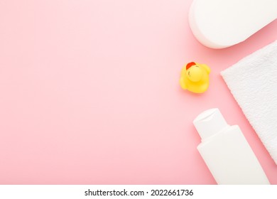 White shampoo bottle, towel, wisp and yellow rubber duck. Things for baby bathing. Closeup. Pastel color. Empty place for text or logo on light pink table background. 