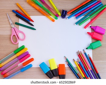 A white sheet of paper lay on a wooden table, near , pencils, markers, pens . The view from the top.