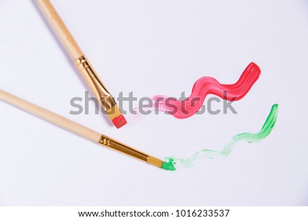 White sheet of paper with two brushes and painted red and green waves, place for the inscription copyspace top view