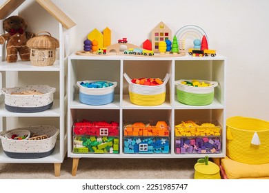 White shelving with colorful storage baskets and transparent boxes in children room. Rainbow toys in stylish baskets and plastic containers. Organizing and Storage Ideas in playroom. Interior design.