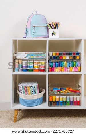 White shelving with kids backpack and various material for creativity and art activity. Stationery and supplies for drawing and craft. Organizing and storage in childrens room. 