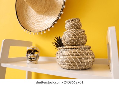 White shelving unit with wicker baskets and sombrero hanging on yellow wall