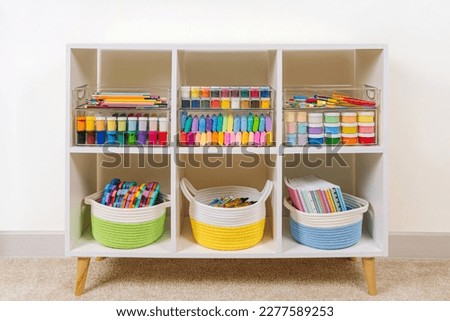 White shelving with various material for creativity and kids art activity. Stationery and supplies for drawing and craft. Organizing and storage in craft room.  