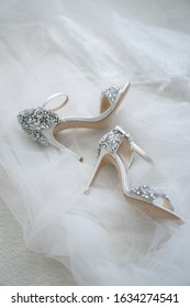 White shoes of the bride in brilliant crystals lie on the veil. Things for an elegant wedding.