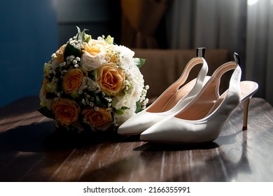 white shoes of the bride on a brown shelf with a bouquet of flowers play of light and shadow. concept for event agencies