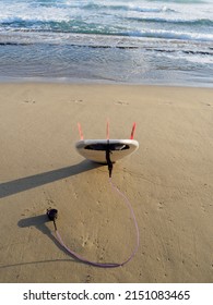 White Short Surfboard With Purple Leash In Sand Ready To Surf.